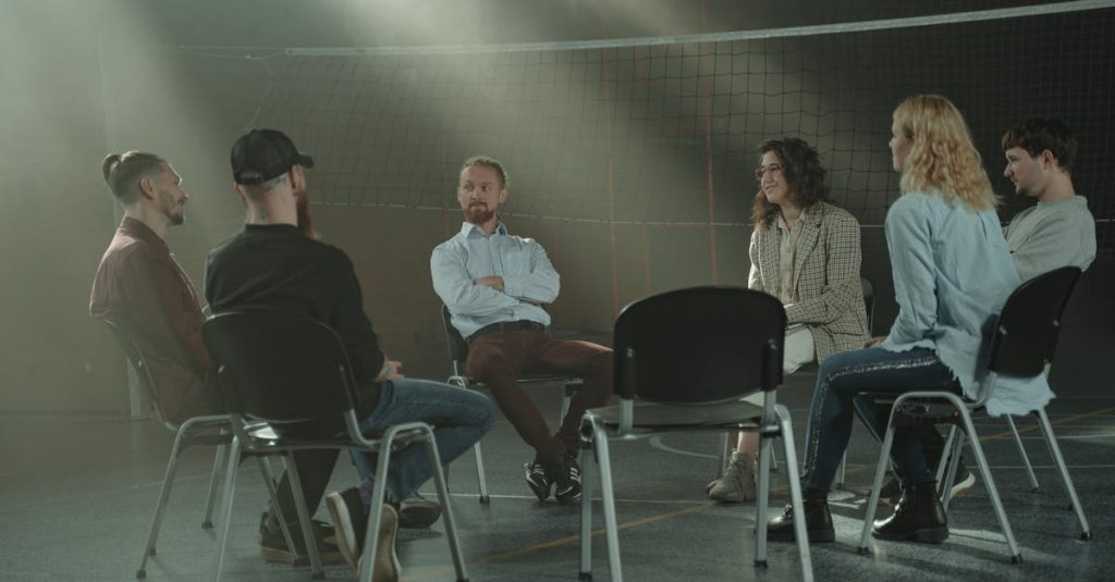 A group therapy session with six adults seated in a circle, discussing support and mental health.